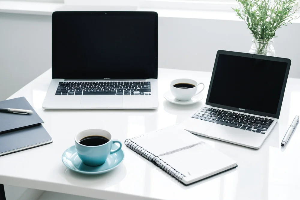 A laptop and phone showing messages on a bright desk
